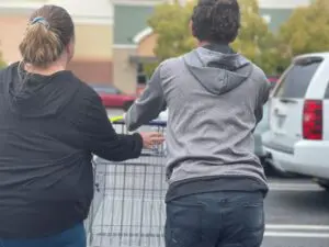 A young man is pushing a shopping cart with his mother in a parking lot