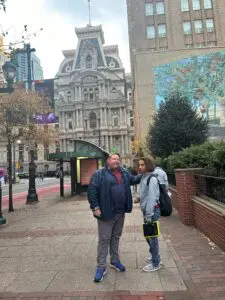 A young man with an AAC device is standing on a city sidewalk with his father.