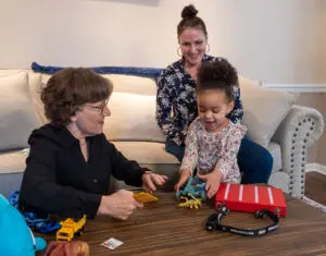 A happy toddler-aged girl is communicating with PECS and receiving dinosaur toys to play with.